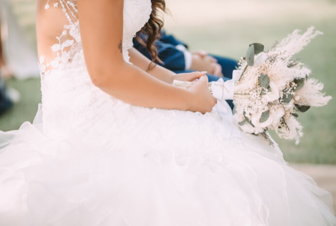 Close-up of bride holding bouquet while sitting in wedding dress outdoors Close-up of bride holding bouquet while sitting in wedding dress outdoors